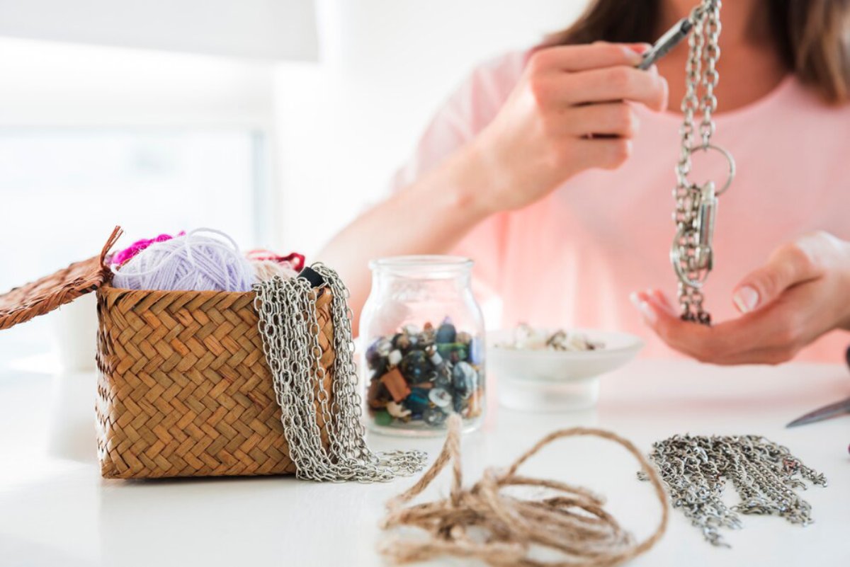 Woman crafting with jewelry and yarn, using tools at a bright crafting table.