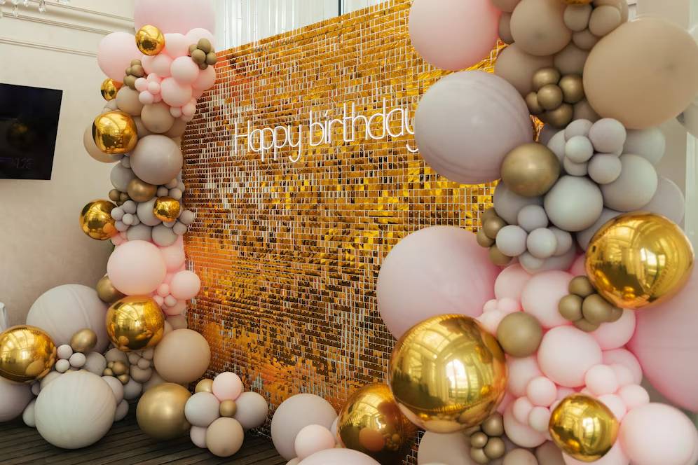 Decorative gold and pink balloon arch surrounding a golden backdrop with the phrase 