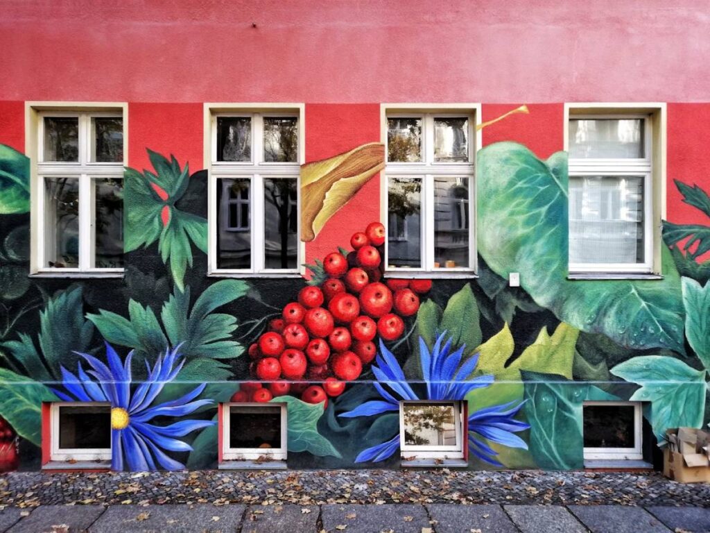 Red building facade with detailed mural of lush greenery and fruit around white-framed windows.