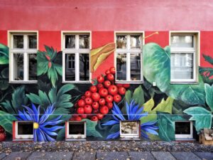Red building facade with detailed mural of lush greenery and fruit around white-framed windows.