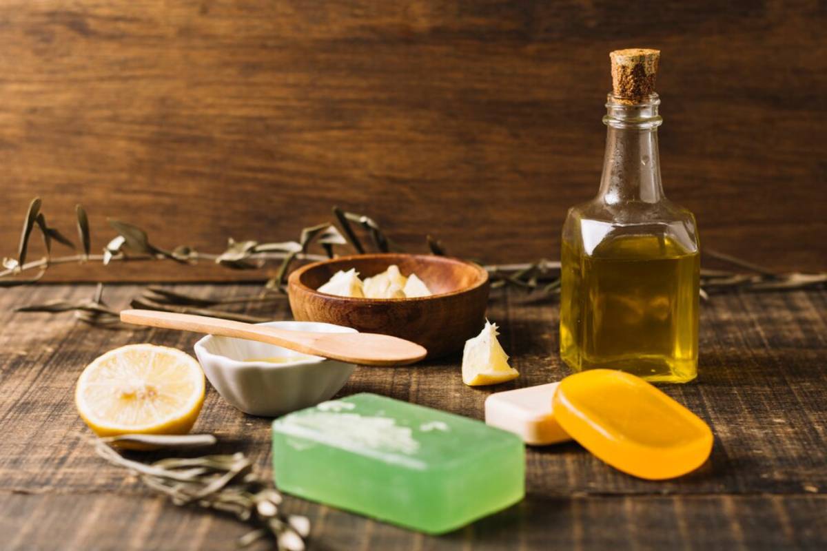Natural skincare products on a wooden surface, including olive oil, lemon, shea butter, and handmade soaps.