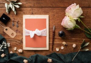 Elegant wedding invitations with floral designs and wax seal on a silver tray, accompanied by pink roses and scattered petals.