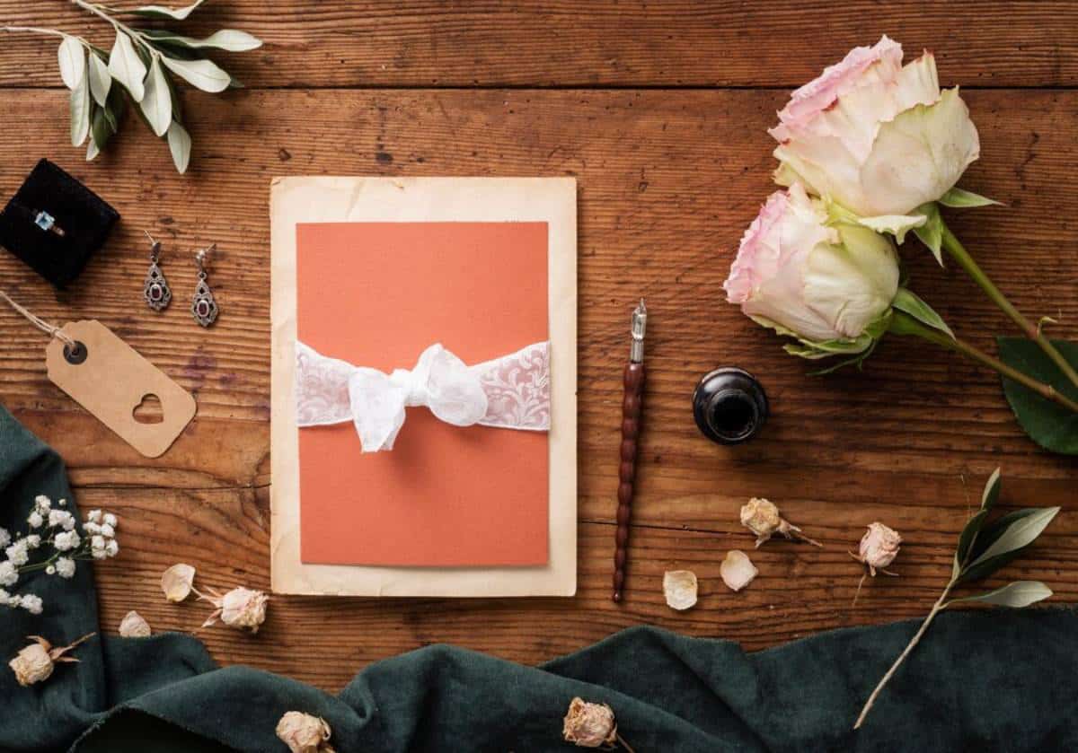 Elegant wedding invitations with floral designs and wax seal on a silver tray, accompanied by pink roses and scattered petals.