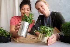 Two women smiling and holding small potted plants at a table.