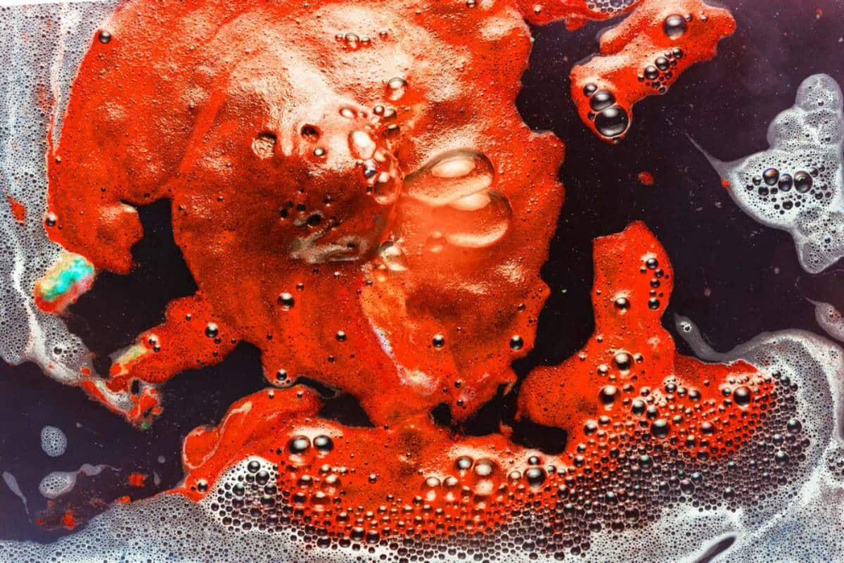 Abstract close-up of vibrant red and black liquid texture with bubbles and frothy details.