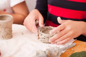 Child shaping a clay pot by hand during a pottery class, demonstrating creativity and tactile learning.