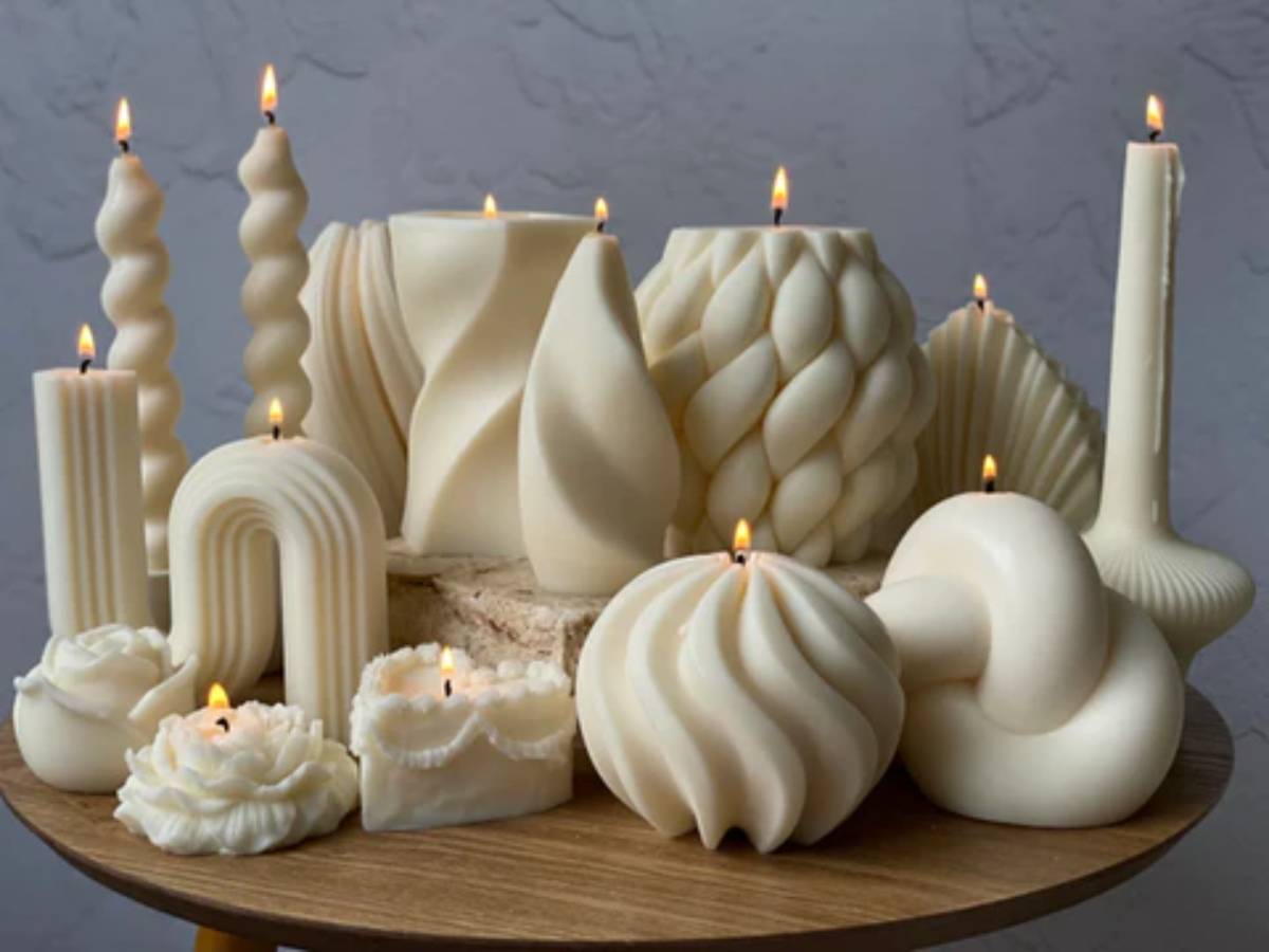 Collection of various uniquely shaped white candles, some lit, displayed on a wooden tray.