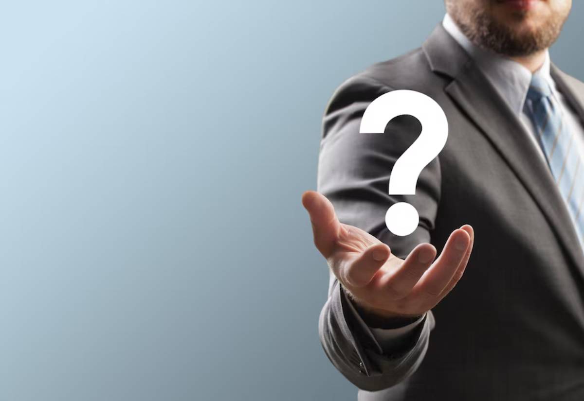 Businessman in a gray suit holding a floating question mark symbol in his hand, symbolizing inquiry or uncertainty.