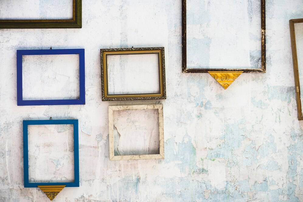 Various empty picture frames on a distressed white wall.