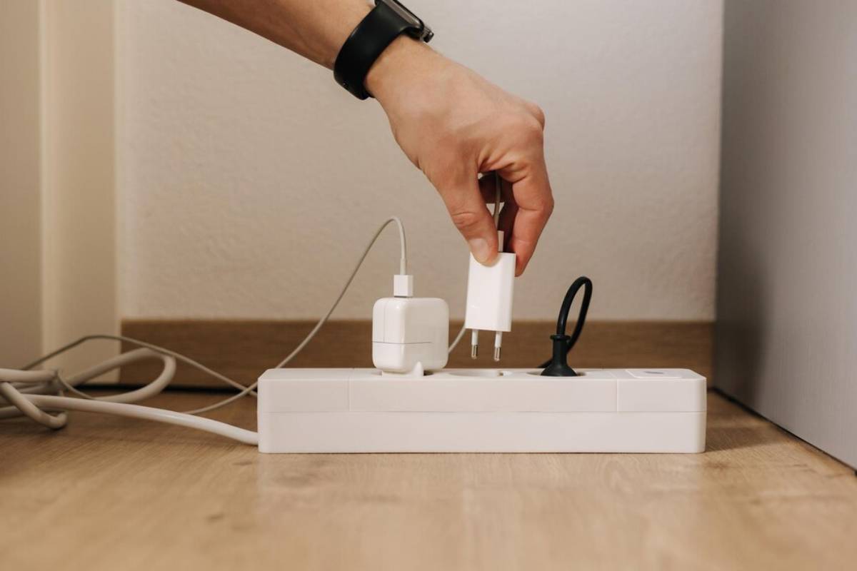Hand plugging a white charger into a power strip on a wooden floor.