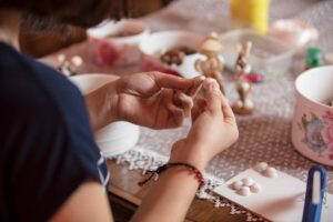 A person engaging in a craft, handling small shells and decorative items on a table.