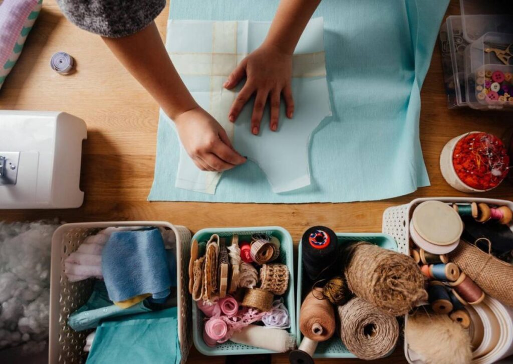 Person tracing pattern on fabric with sewing accessories and materials nearby on a wooden table.