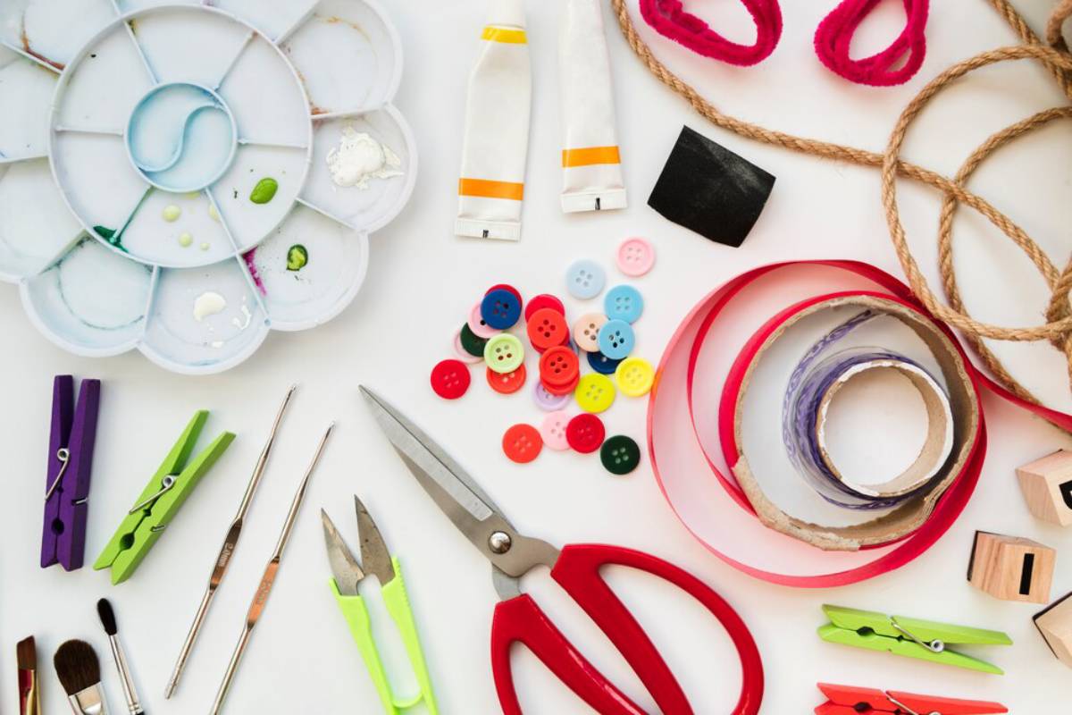 Assorted craft supplies including scissors, paint, ribbons, and buttons spread on a white surface.