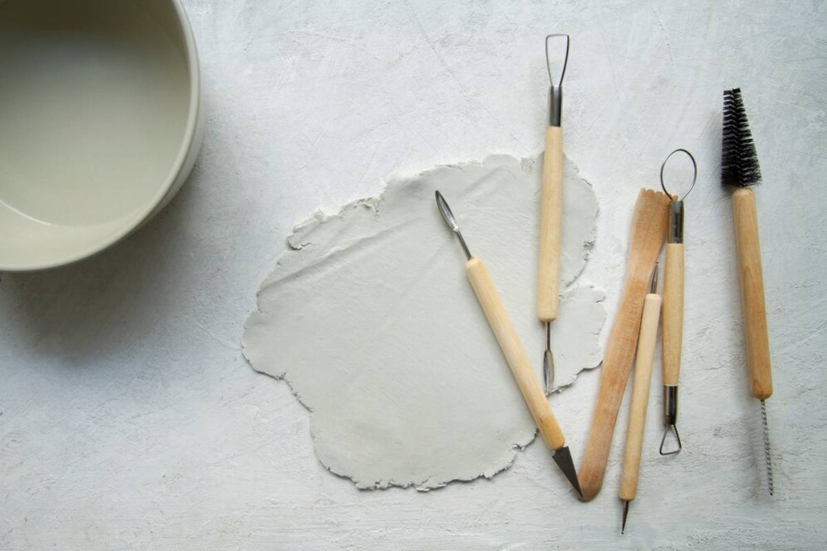 Assorted pottery tools arranged beside a clay slab on a textured surface.