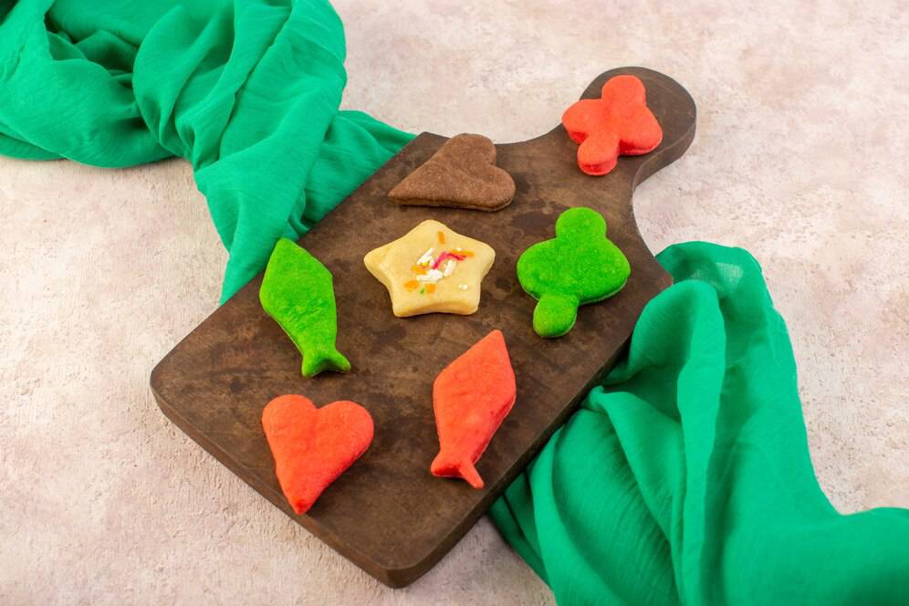 Colorful shaped cookies on a wooden board, with a green fabric.