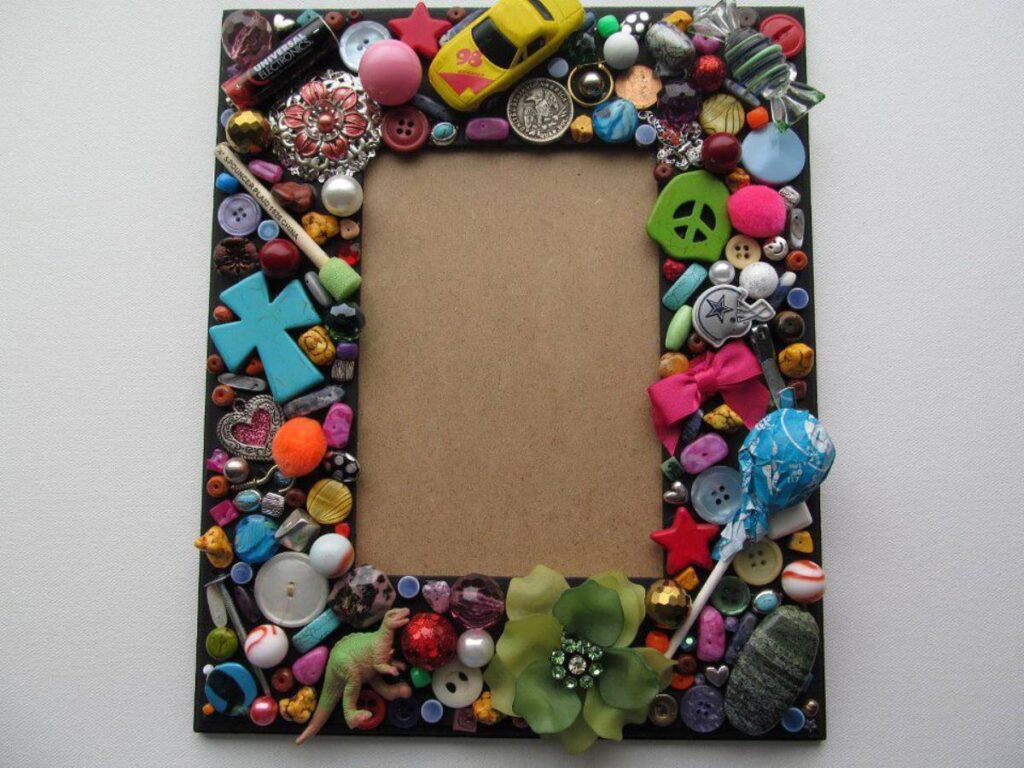 A picture frame decorated with colorful assorted buttons, toys, and trinkets surrounding a blank rectangular space.