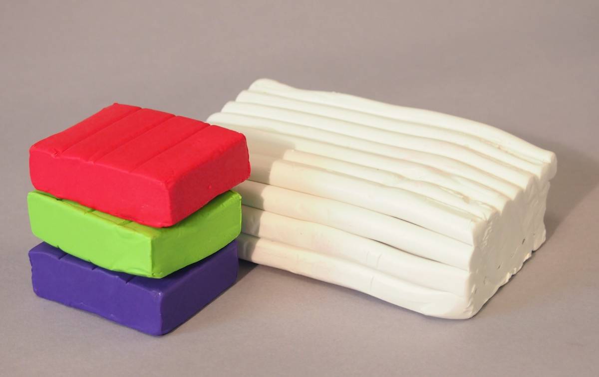 A stack of colorful plasticine blocks next to a group of white modeling clay bars on a gray background.