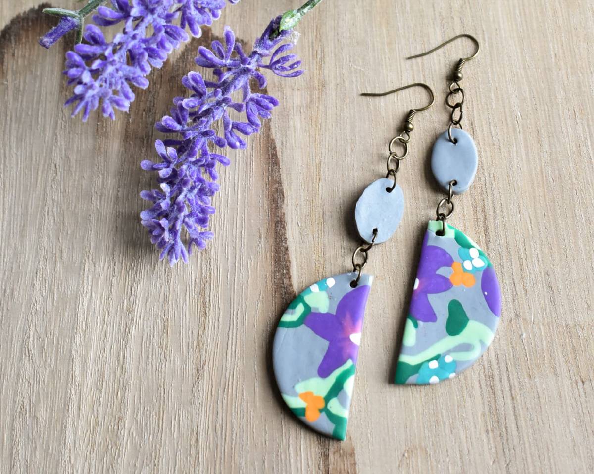 Handcrafted earrings with floral pattern next to artificial lavender on a wooden surface.