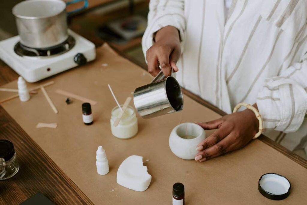 Person pouring liquid into a candle container in a candle-making workshop.