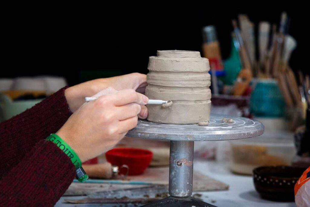 Person sculpting a clay pot on a pottery wheel, surrounded by art tools.