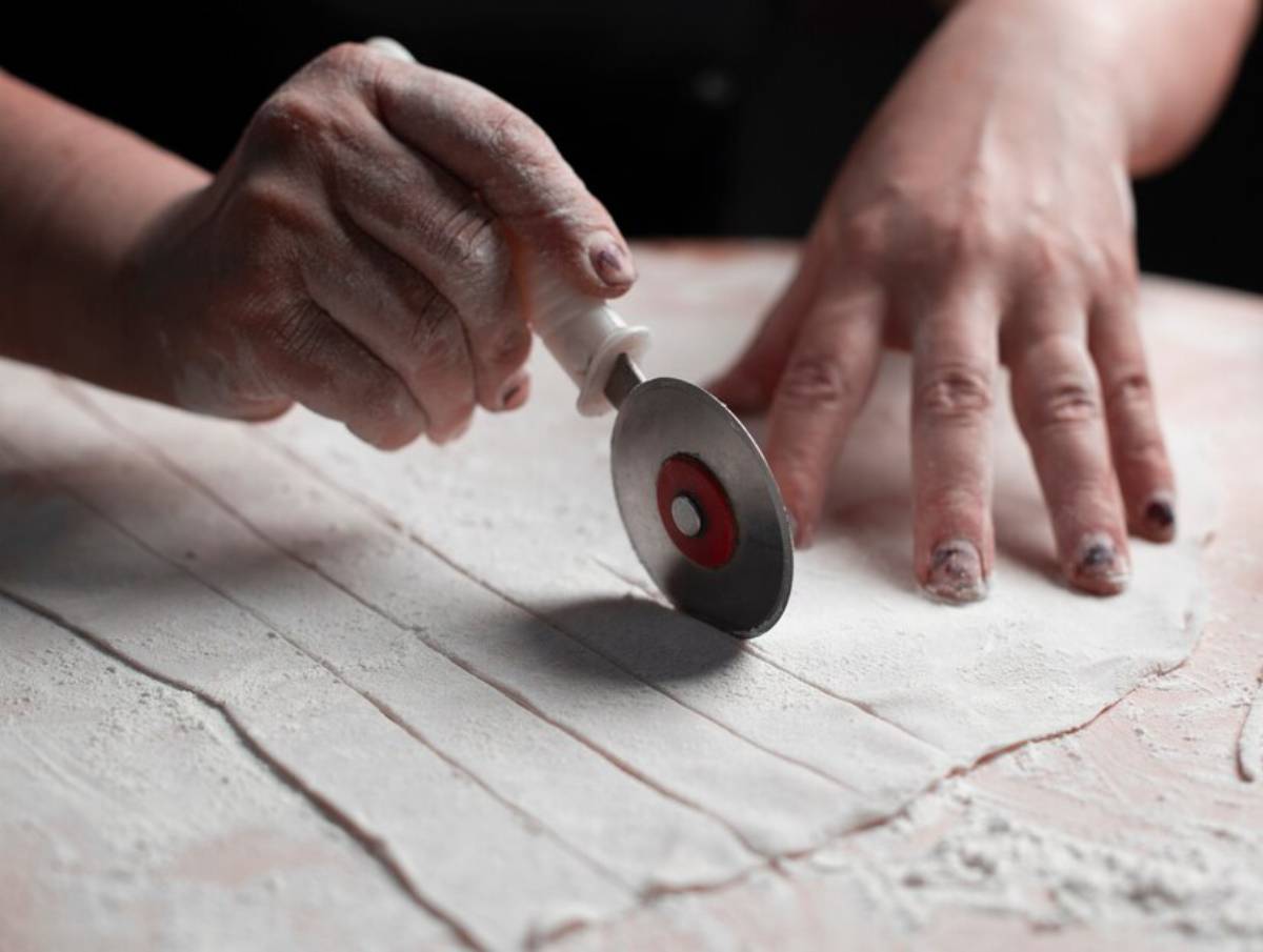 Close-up of hands cutting a slab of clay with a circular cutting tool.