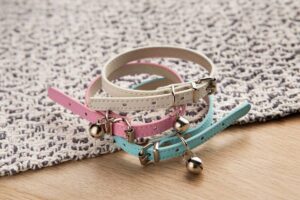 Three colorful cat collars with bells on a textured rug.