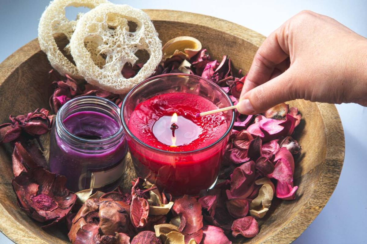 A hand lighting a candle in a bowl surrounded by dried flowers and colorful wax jars.