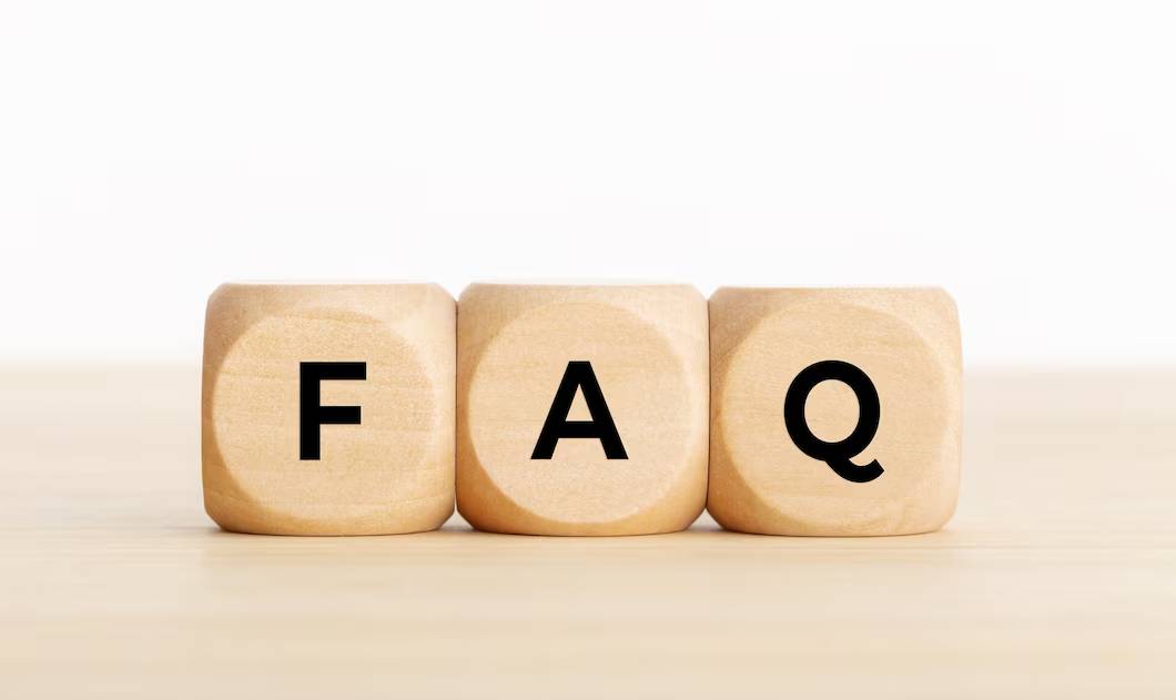 Three wooden blocks on a table spelling FAQ against a pale background.