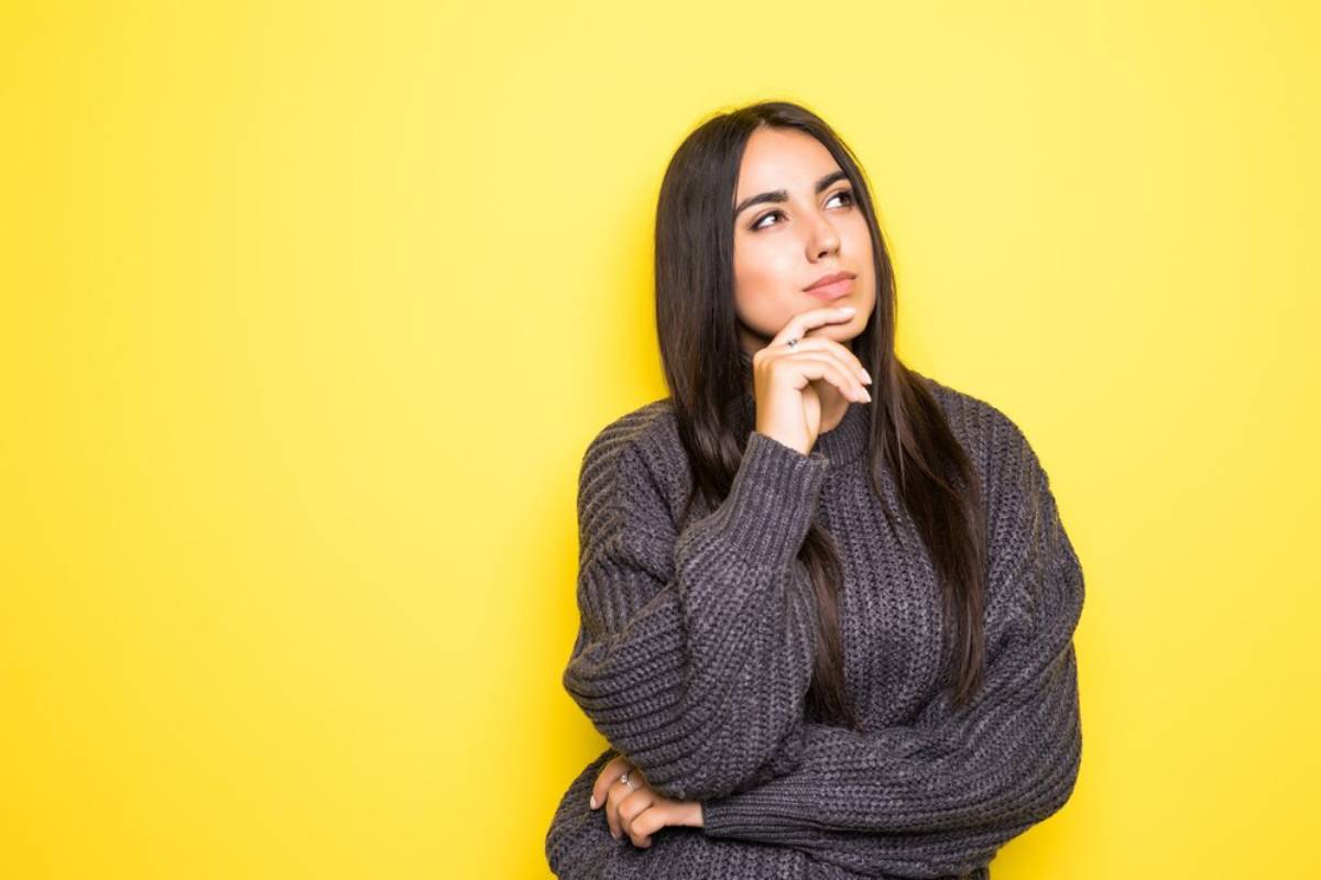 Woman in gray sweater pondering, with yellow background.