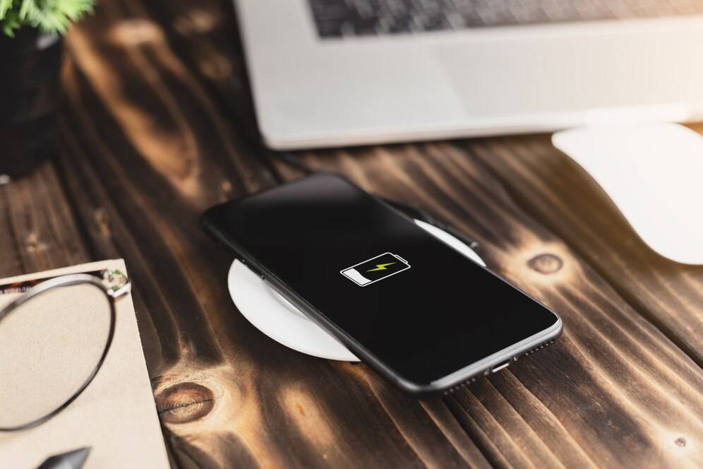 Smartphone on a glowing, wireless charging pad emitting a turquoise light in a dark room.